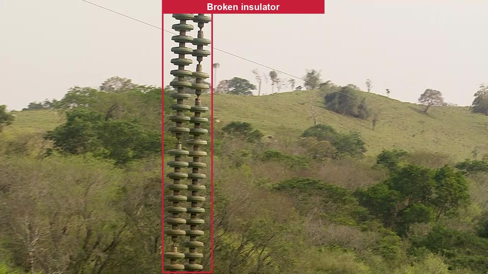 Annotated drone photograph of a ceramic disc insulator string with a bounding box around a visible crack, labelled Broken insulator.